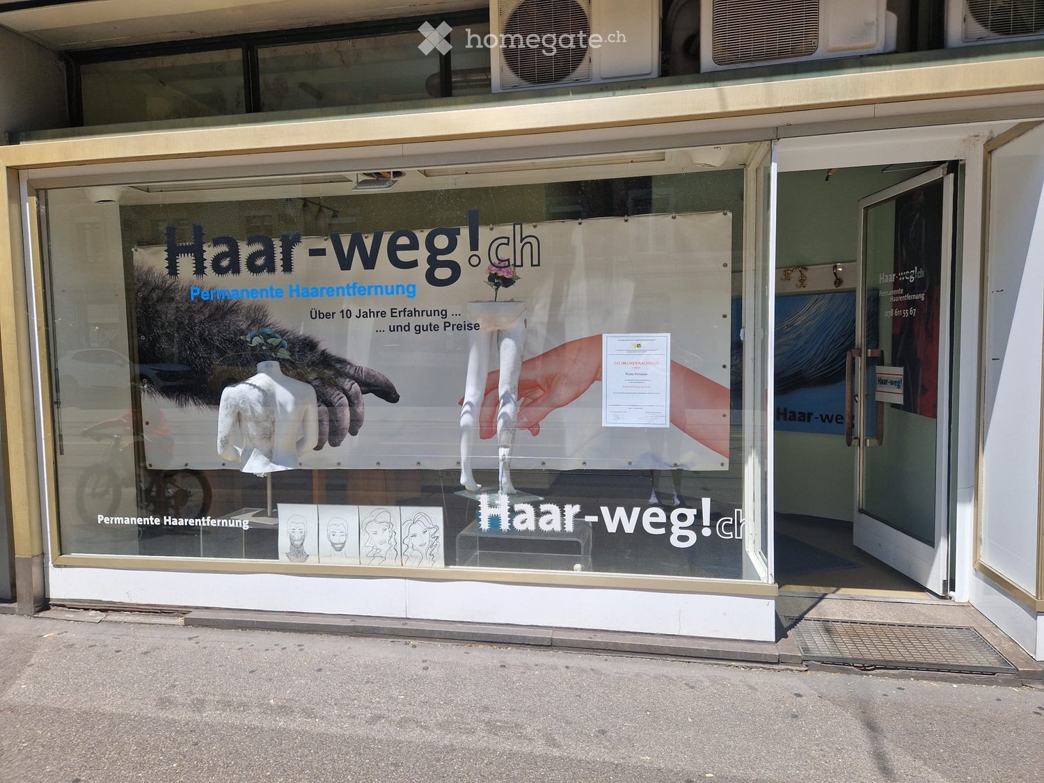Storefront with large glass windows displaying advertisements for permanent hair removal, including mannequins and illustrations.
