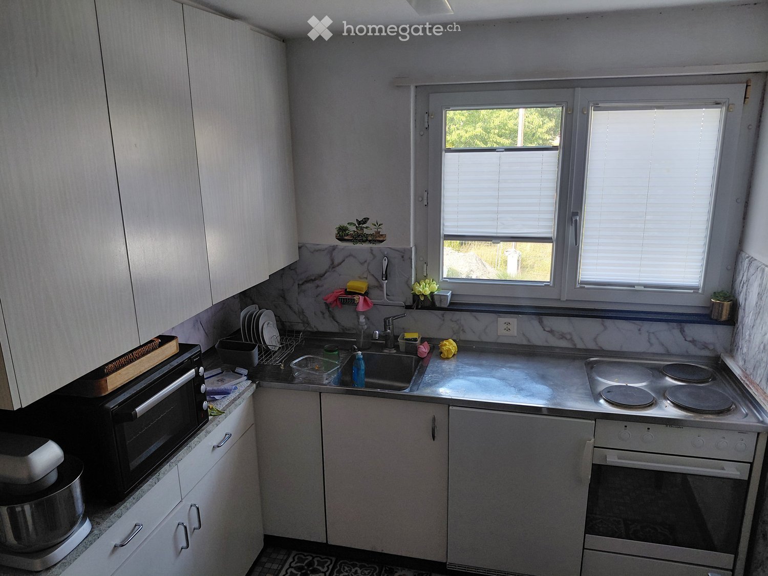Modern kitchen with white cabinets, marble countertops, and stainless steel appliances including a microwave, oven, and sink.