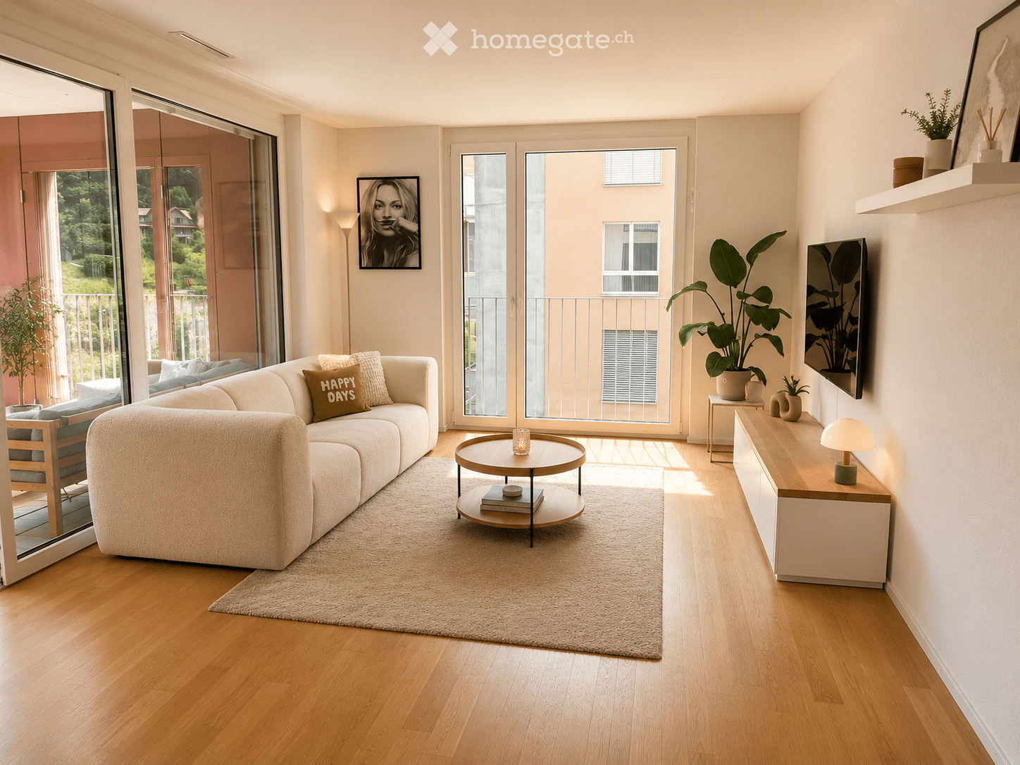 Modern living room with light wood flooring, large windows, a white sectional sofa, a round coffee table, side tables, and decorative plants.
