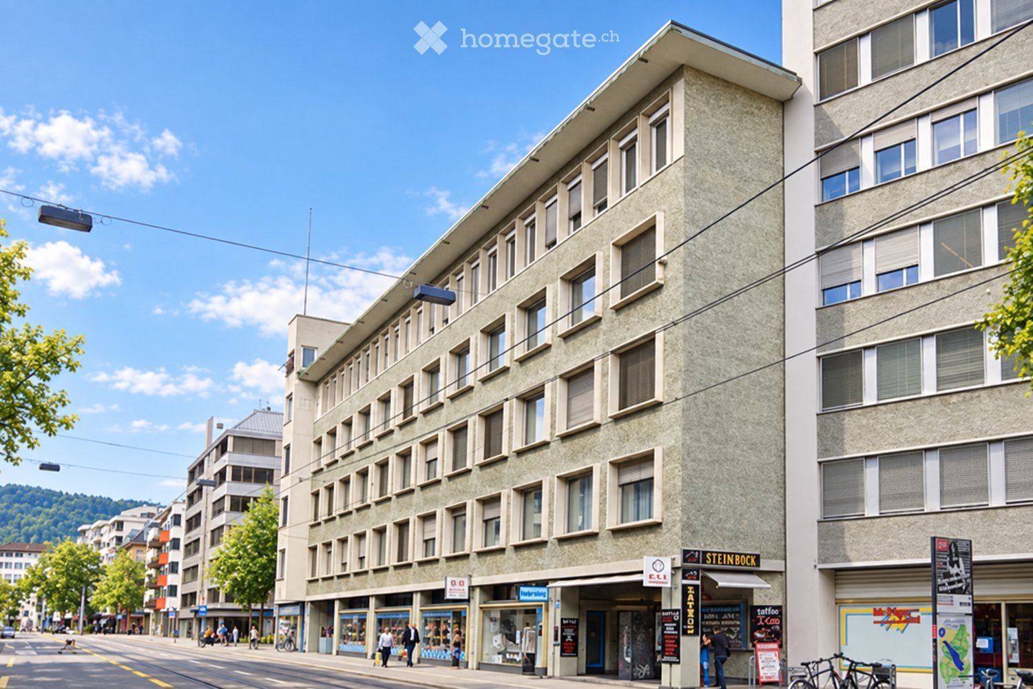 Multi-story building with a modern facade, multiple windows, and commercial storefronts at the ground level. The building is situated on a busy urban street with pedestrians and bicycles visible.