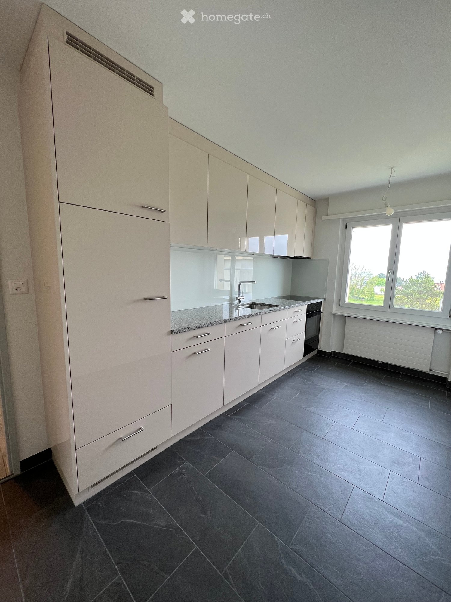 Modern kitchen with white cabinets, granite countertop, dark tiled floor, and large windows.