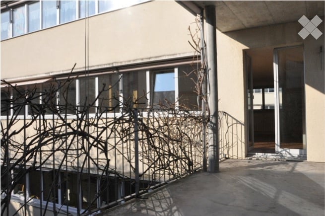 Balcony with metal railing, overlooking a building with large windows and a staircase leading up.