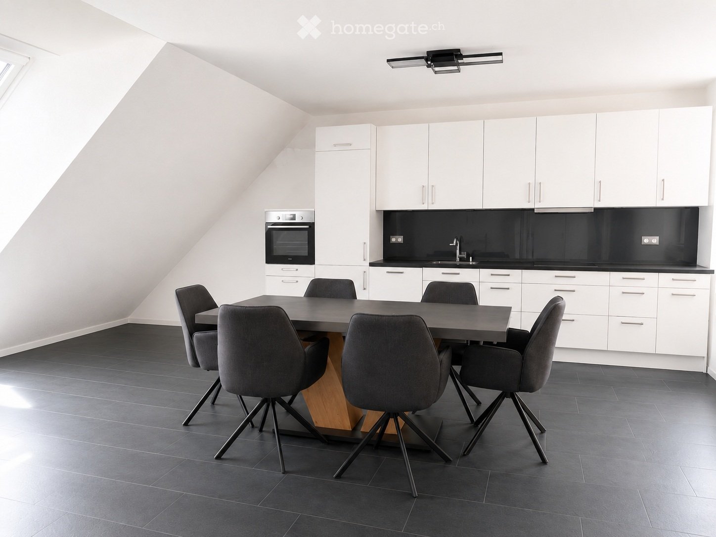 Modern kitchen with white cabinets, black countertops, a sink, an oven, and a dining table with four chairs.