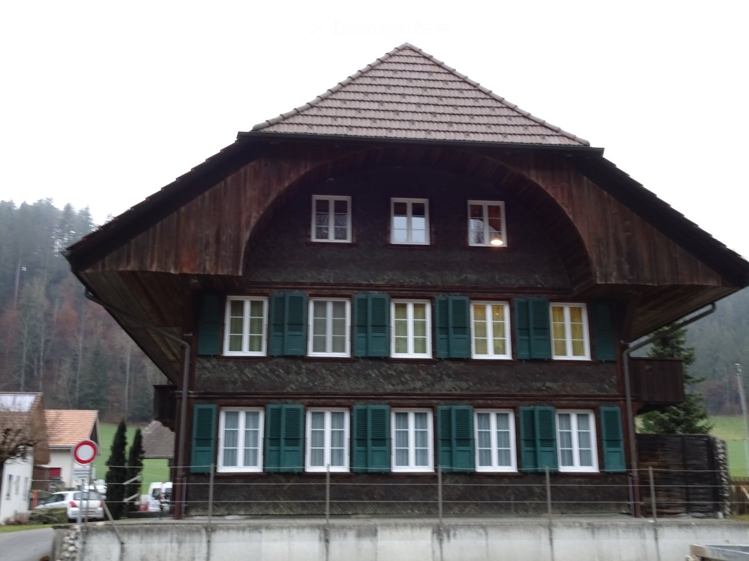 Traditional wooden house with multiple windows, green shutters, and a steeply pitched roof.