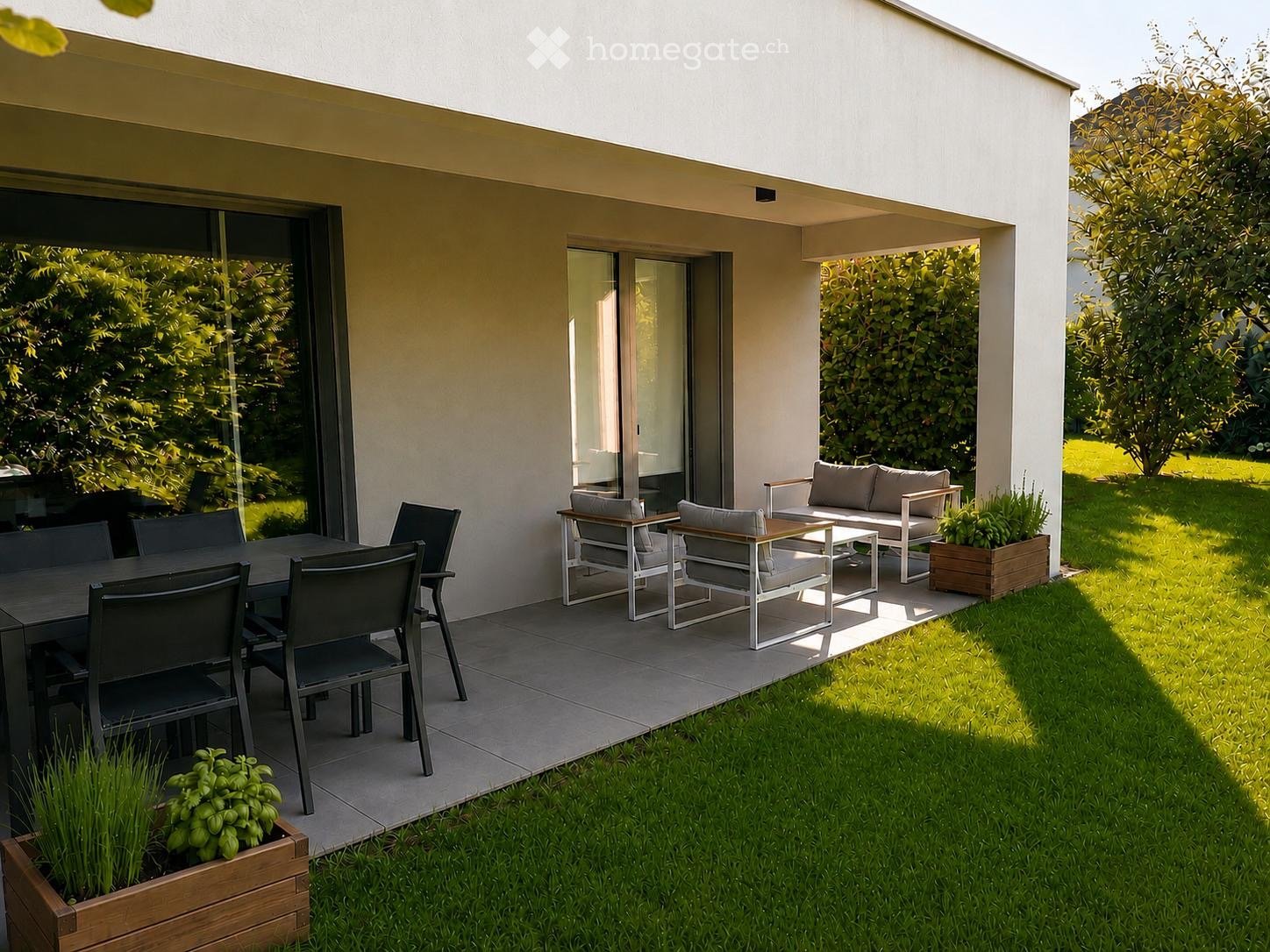 Modern outdoor patio with a dining table and chairs, a sofa set, and potted plants, surrounded by a well-maintained lawn and trees.