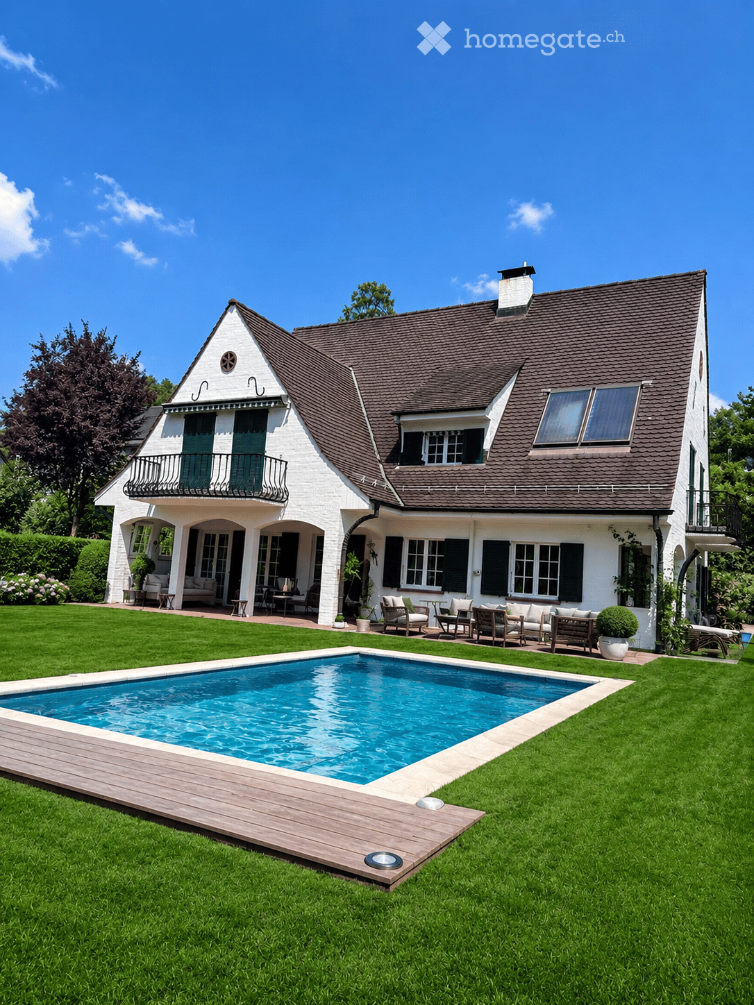 Two-story white house with dark brown roof, multiple windows, balconies, and a swimming pool in the front yard.