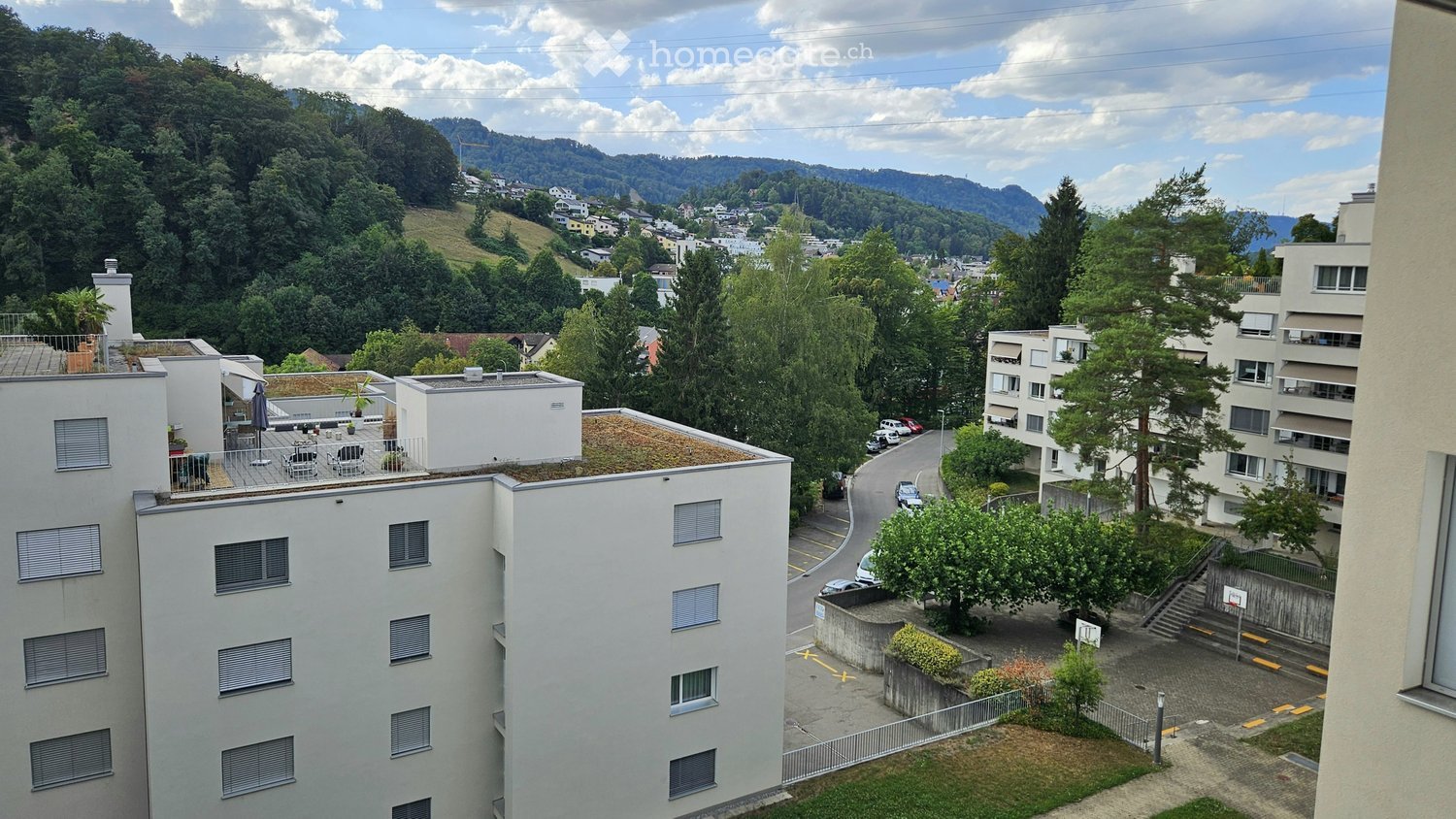View from a rooftop terrace showing multiple apartment buildings, green hills, and a town in the distance.
