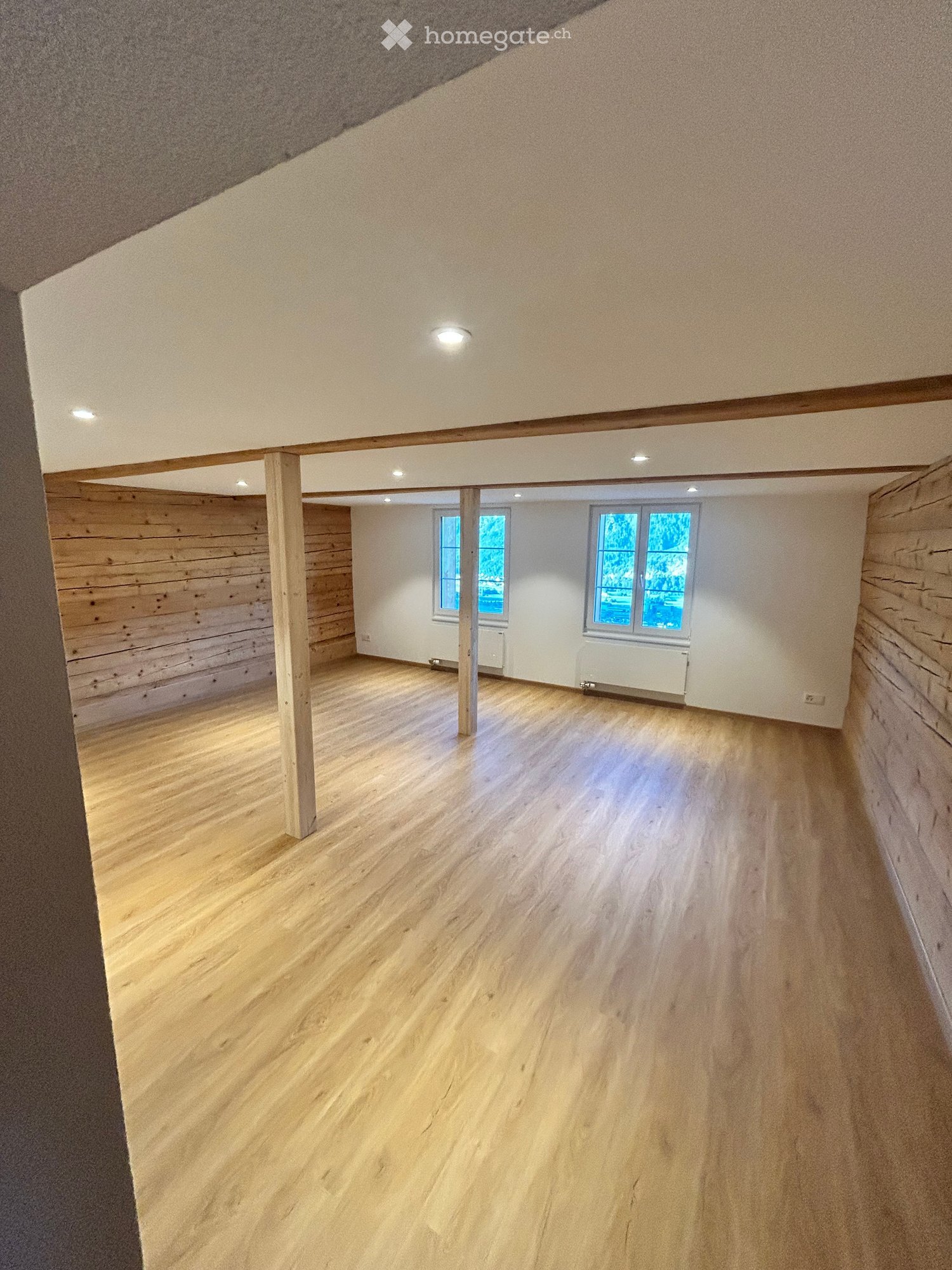 Empty room with wooden flooring, white walls, and large windows. No furniture or equipment present.