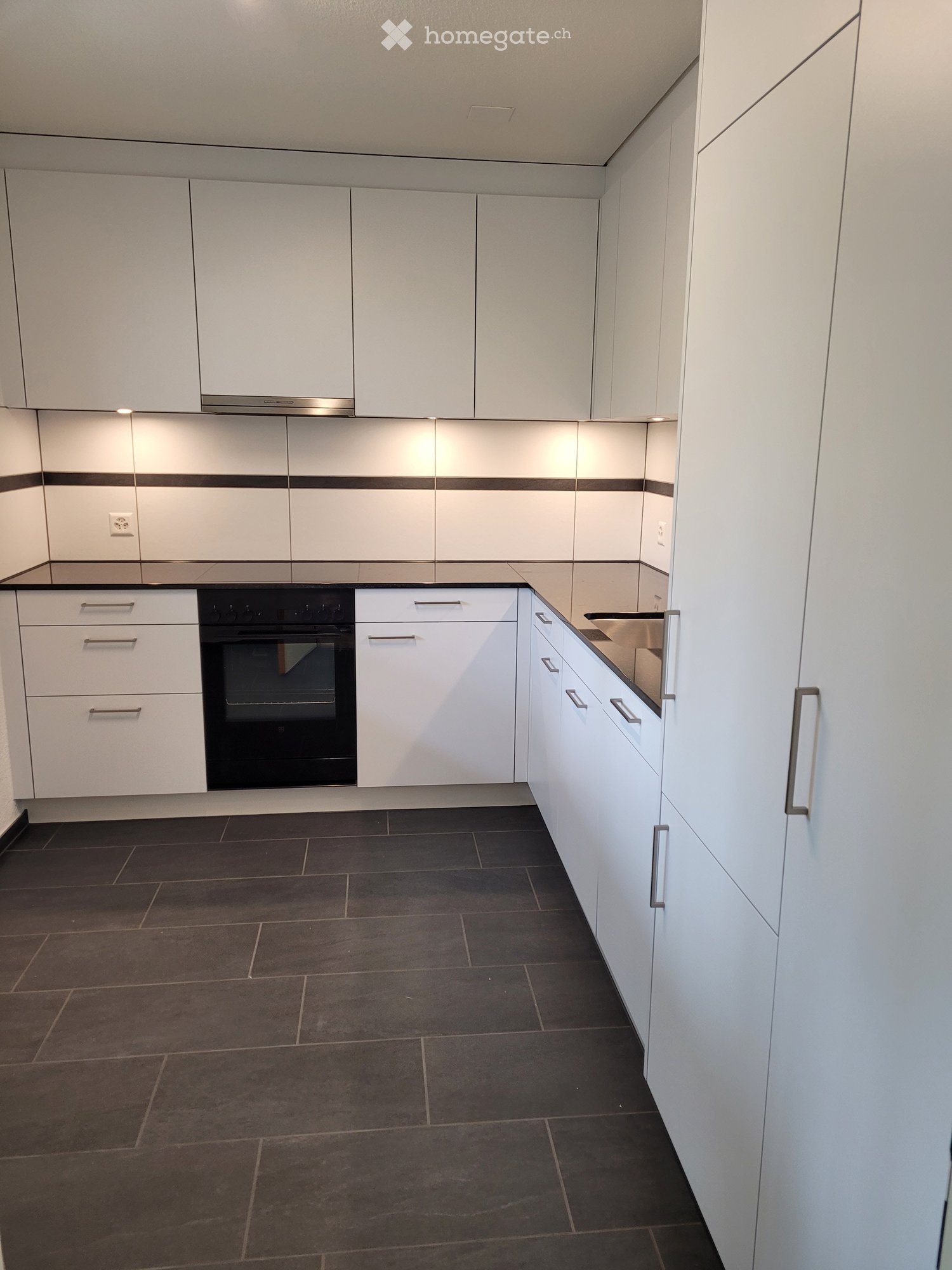Modern kitchen with white cabinets, dark tiled floor, and built-in oven.
