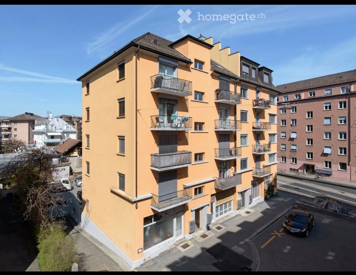 Multi-story residential building with yellow facade, multiple balconies, and surrounding urban environment.