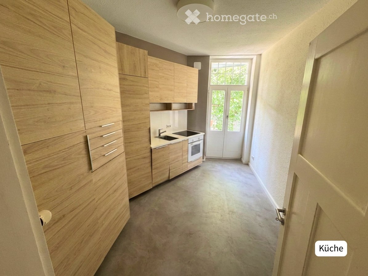 Modern kitchen with light wooden cabinets, a sink, and an oven. The space is bright with large windows and a clean, minimalist design.