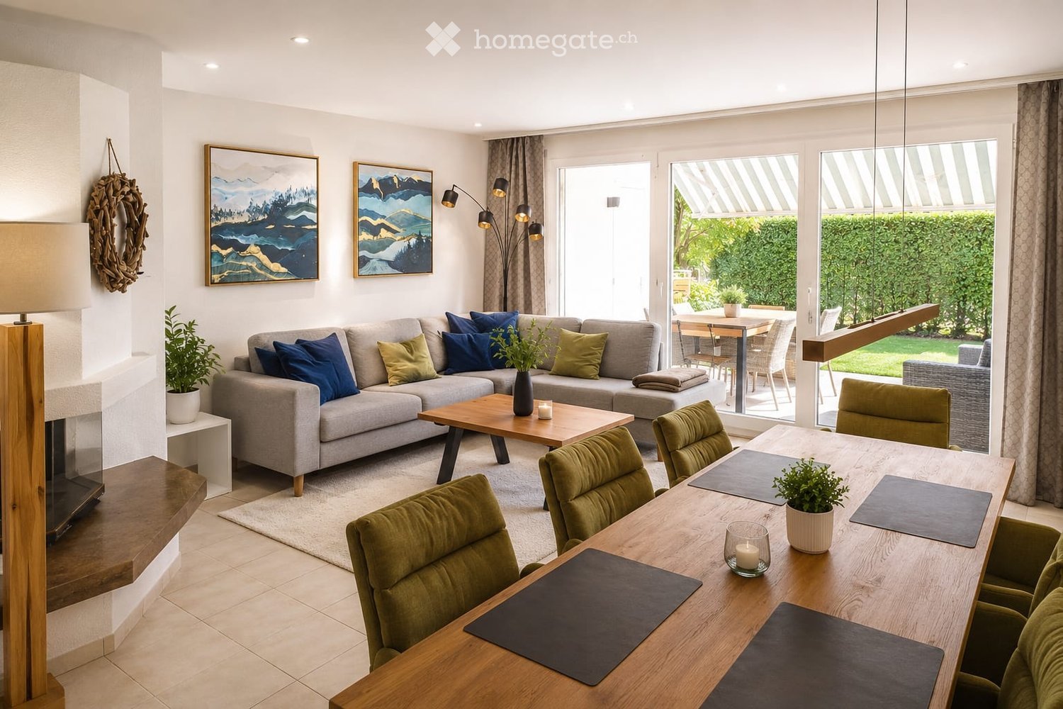 Modern living room with a grey sectional sofa, wooden coffee table, dining table with green chairs, floor lamp, fireplace, and artwork on the walls.