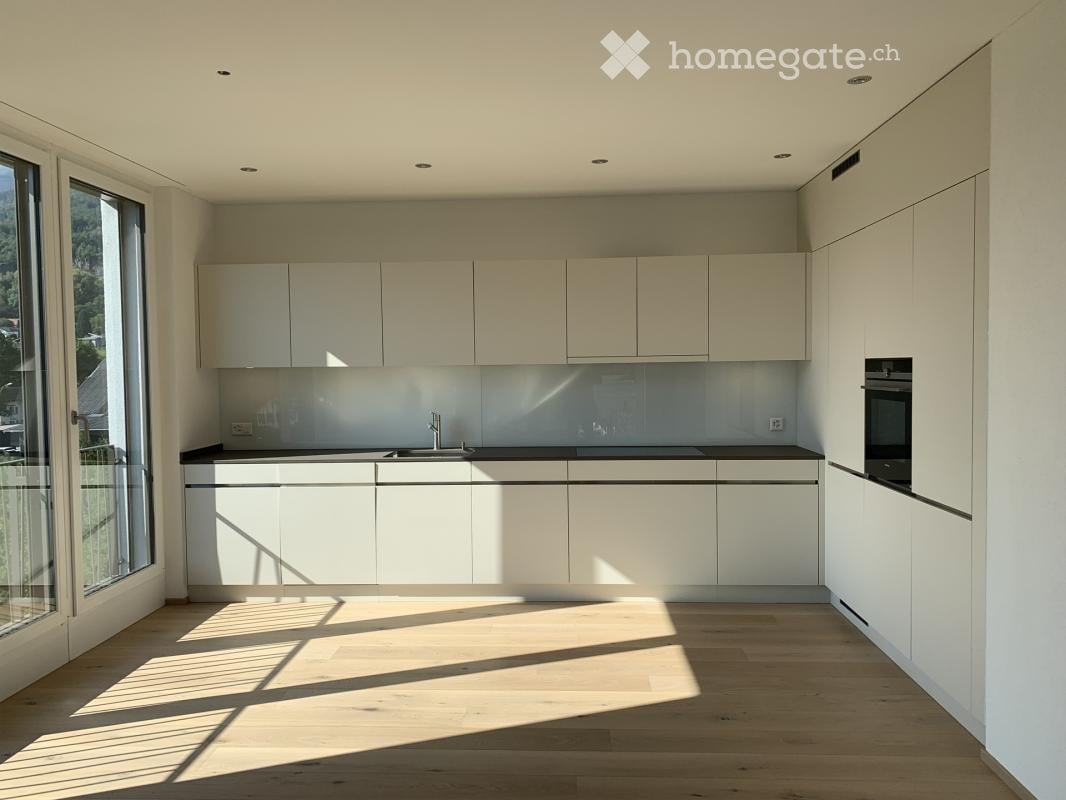 Modern kitchen with white cabinets, a black countertop, and a large window offering a scenic view. The space features a sleek sink, a faucet, and an oven, all illuminated by natural light.