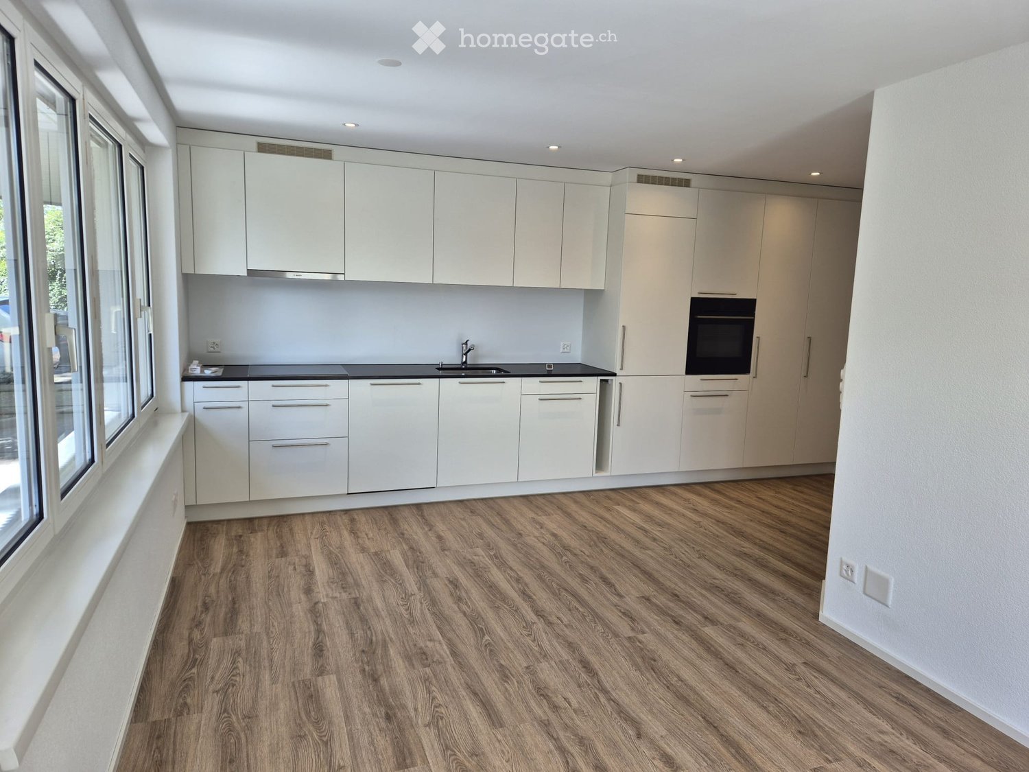 Modern kitchen with white cabinets, black countertops, and wooden flooring. Features a sink, oven, and ample storage space.
