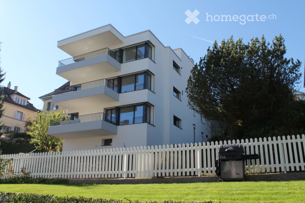 Modern multi-story apartment building with white exterior, large windows, and multiple balconies.