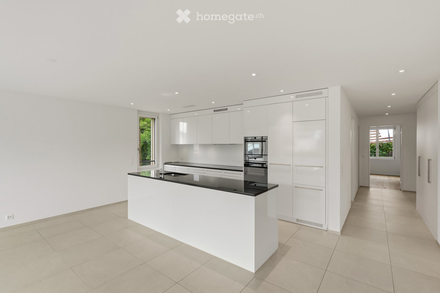 Modern, minimalist kitchen with white cabinets, a black countertop, and built-in appliances including an oven and sink.