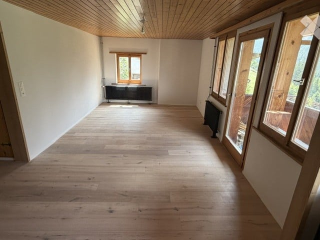 Completely empty room with wooden flooring, white walls, and large windows. No furniture or equipment.
