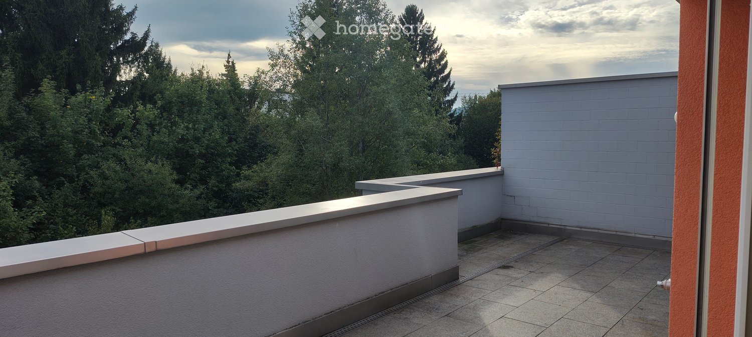 Balcony with tiled floor, white railing, and a view of green trees and a cloudy sky.