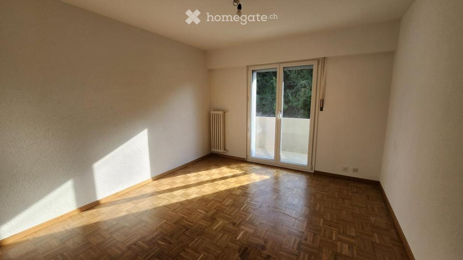 Empty room with wooden flooring, white walls, and a large sliding glass door leading to a balcony.
