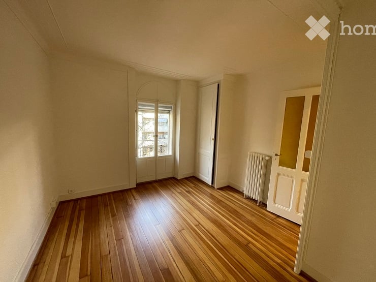 Empty room with wooden flooring, white walls, and a radiator. Features a door with glass panels and a window with frosted glass.