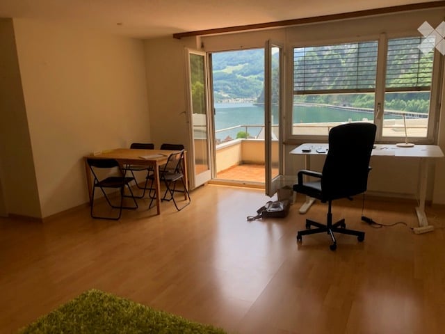 Bright room with wooden flooring, large windows offering a scenic view, a dining area with a table and chairs, and a workspace with a desk and chair.