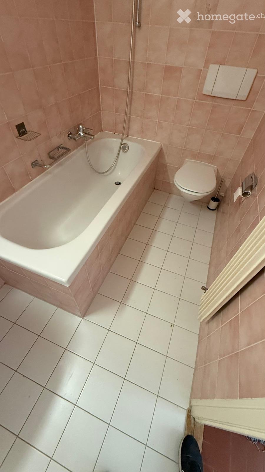 Bathroom with a bathtub, toilet, tiled walls, and a shower hose attached to the wall.