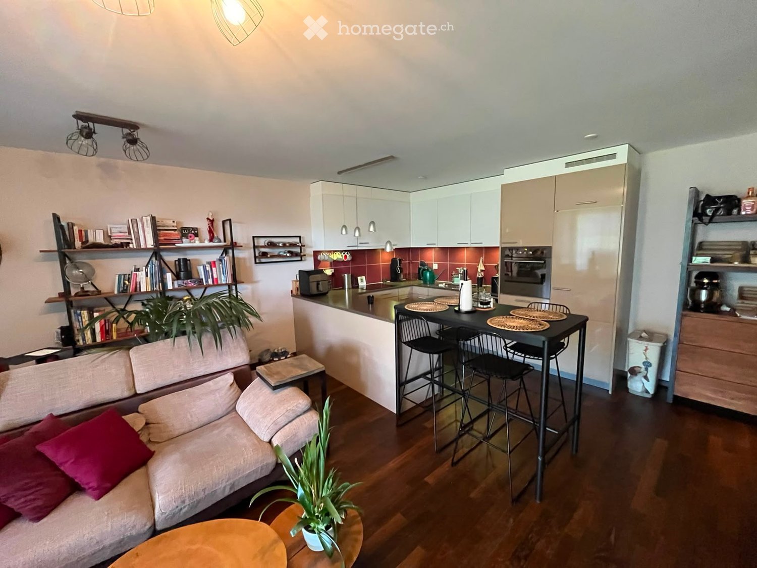 A modern, open-concept living and dining area with a sofa, coffee table, dining table, and kitchen appliances.