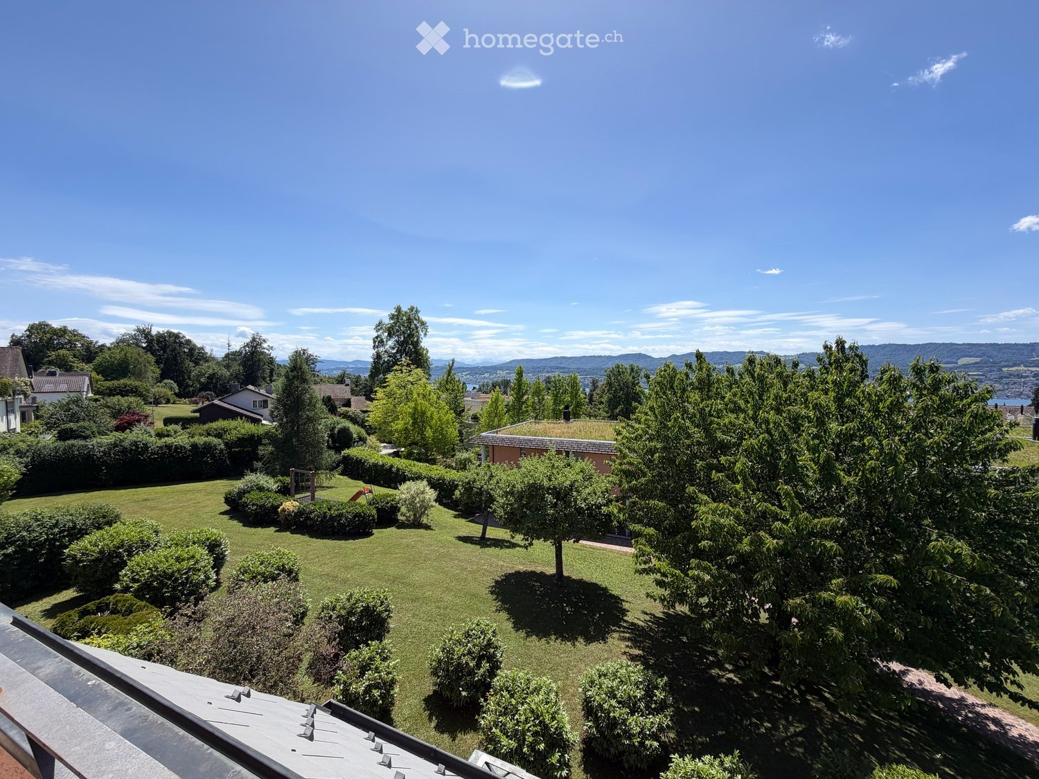 Well-maintained garden with neatly trimmed hedges, trees, and a clear view of the surrounding landscape and distant mountains.