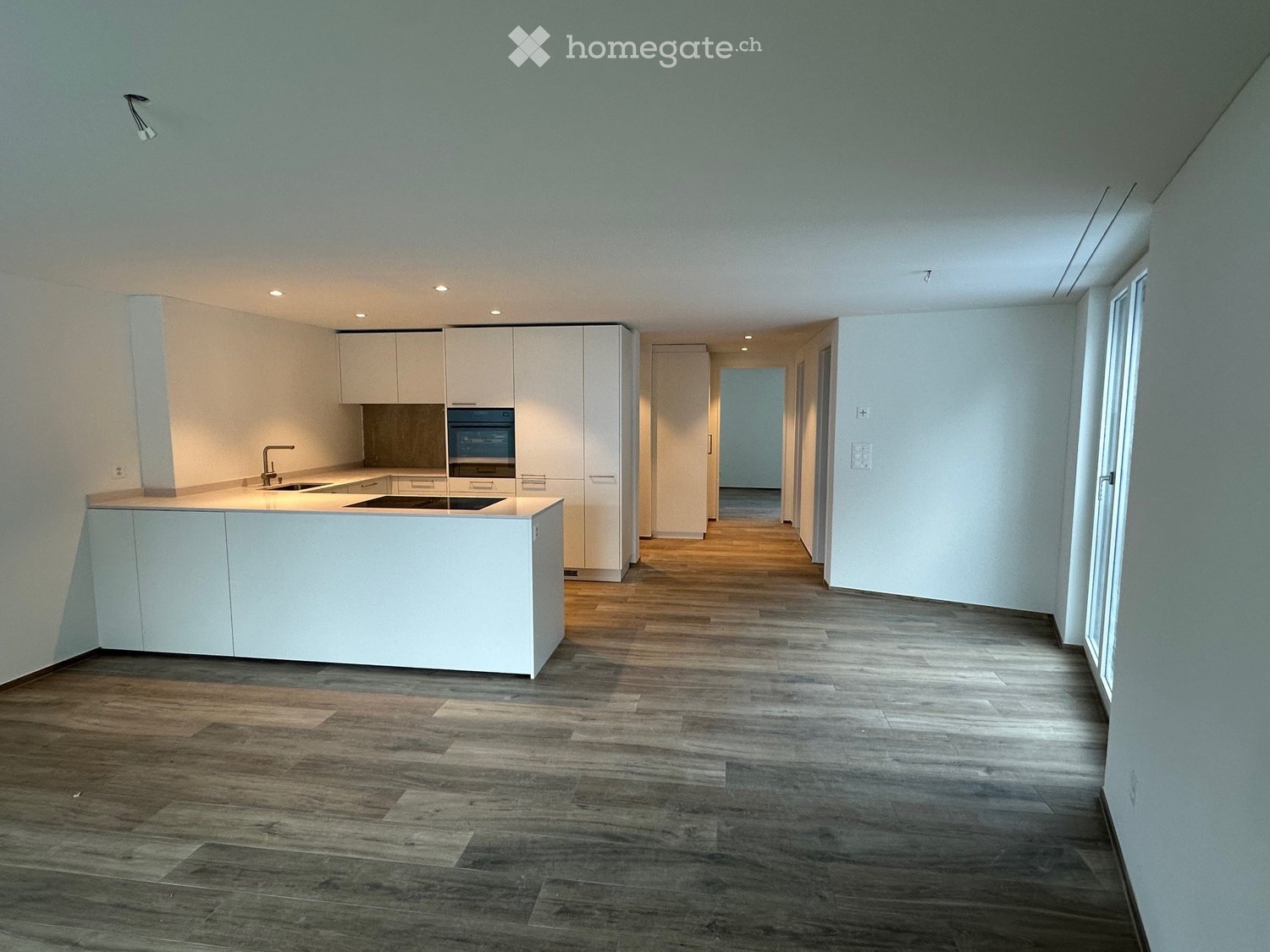 Empty kitchen with white cabinets, a central island, and wooden flooring. No furniture or appliances are present.