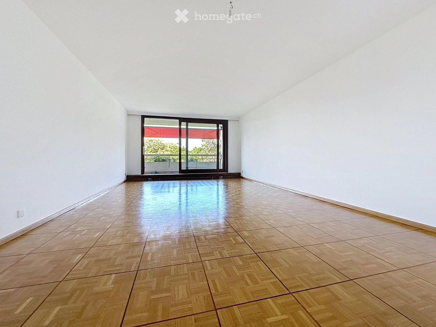 Empty room with wooden parquet flooring, white walls, and large sliding glass door leading to a balcony.