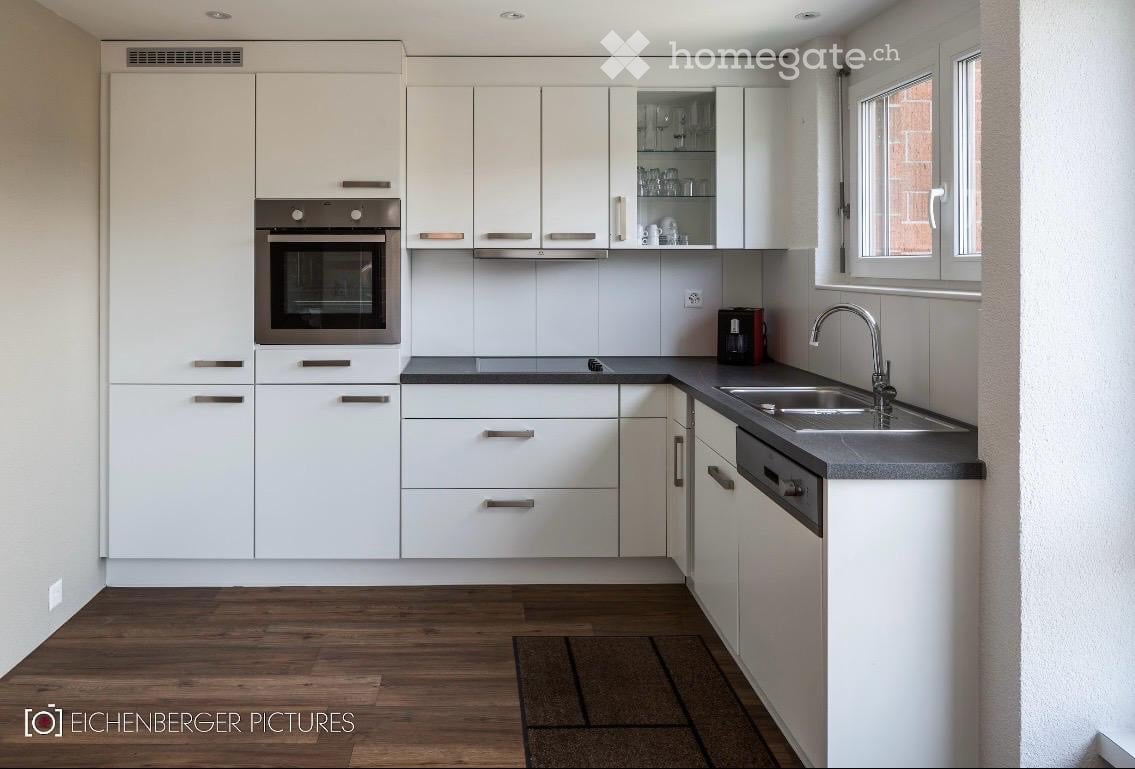 Modern kitchen with white cabinets, stainless steel oven, sink, and faucet, along with a coffee maker on the counter.