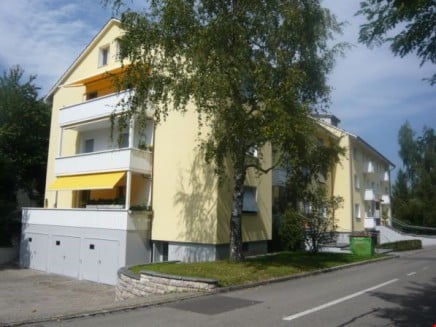 Multi-story residential building with yellow facade, balconies, and a garage.