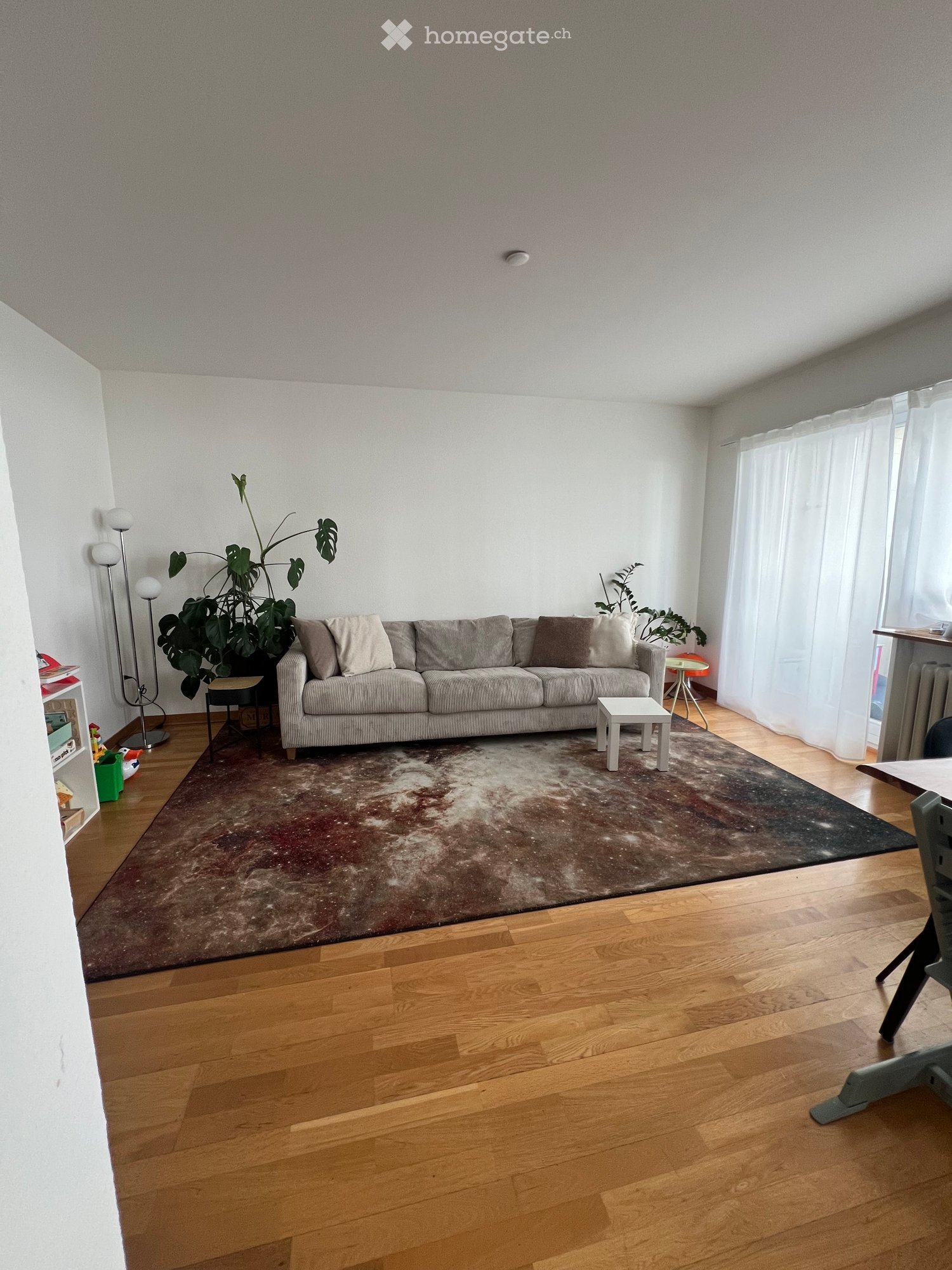 Living room with wooden flooring, large sofa, coffee table, side tables, floor lamp, and plants.