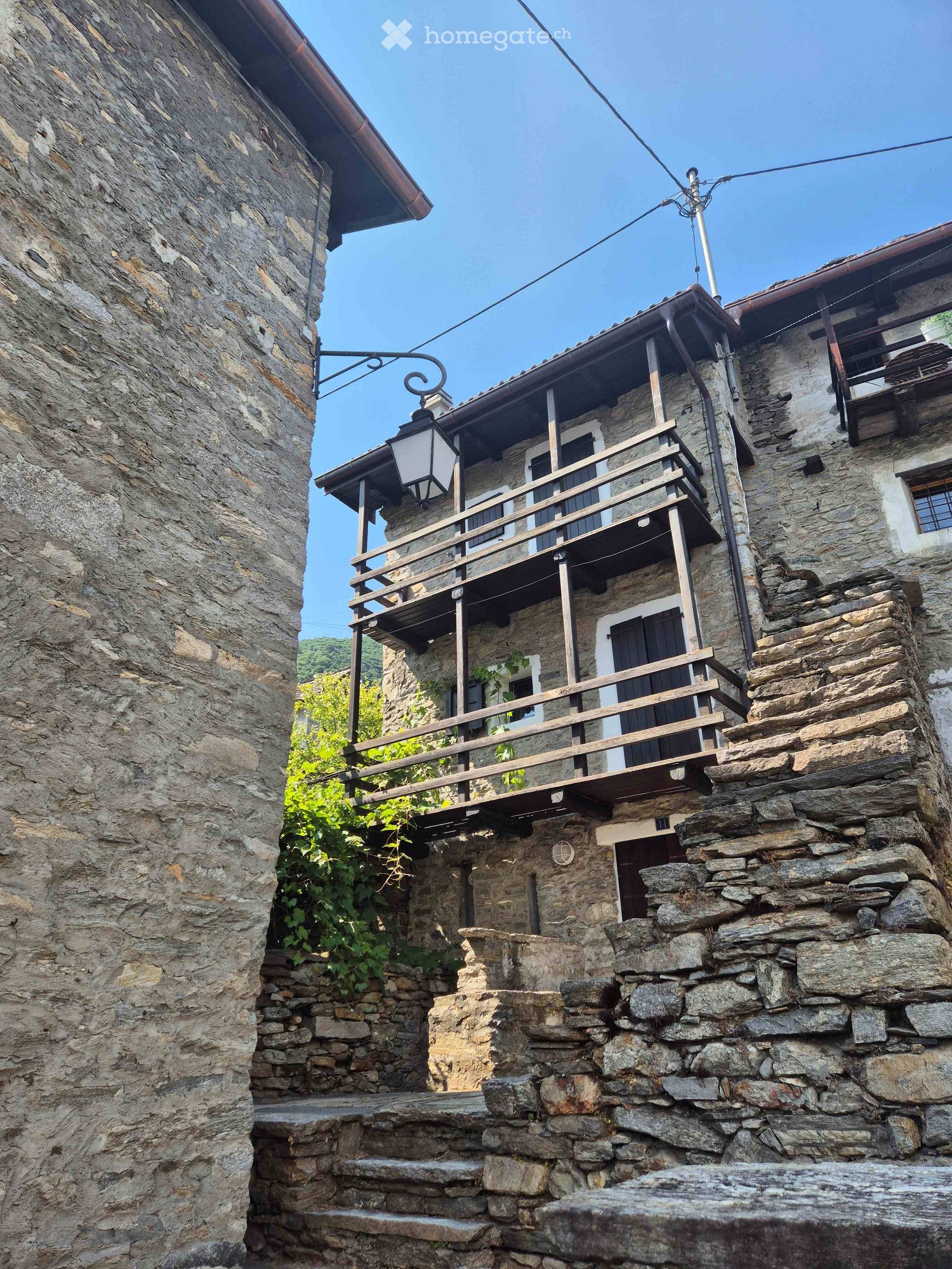 Stone building with wooden balcony and steps leading up to entrance.