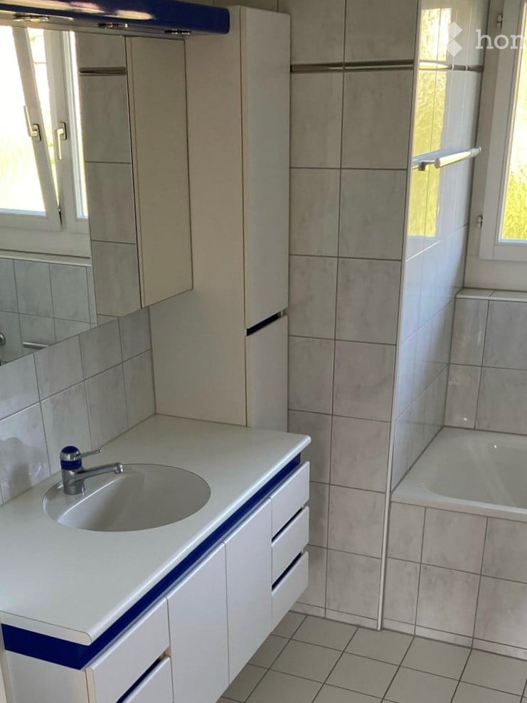 Modern bathroom with a white countertop sink, blue accents, a large mirror, and a bathtub with a glass shower enclosure.