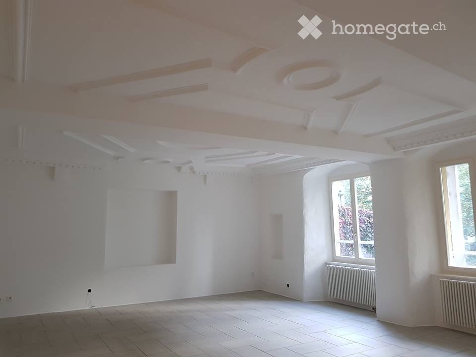 Empty room with white walls, wooden floor, large windows, and radiators. No furniture or equipment present.