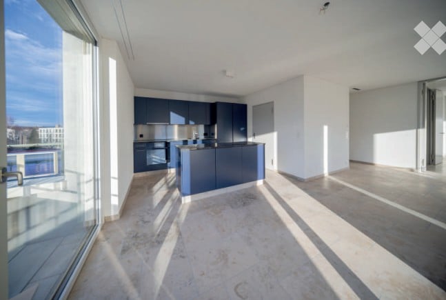 Modern kitchen with dark blue cabinets, a central island, and large windows offering a view of the balcony.