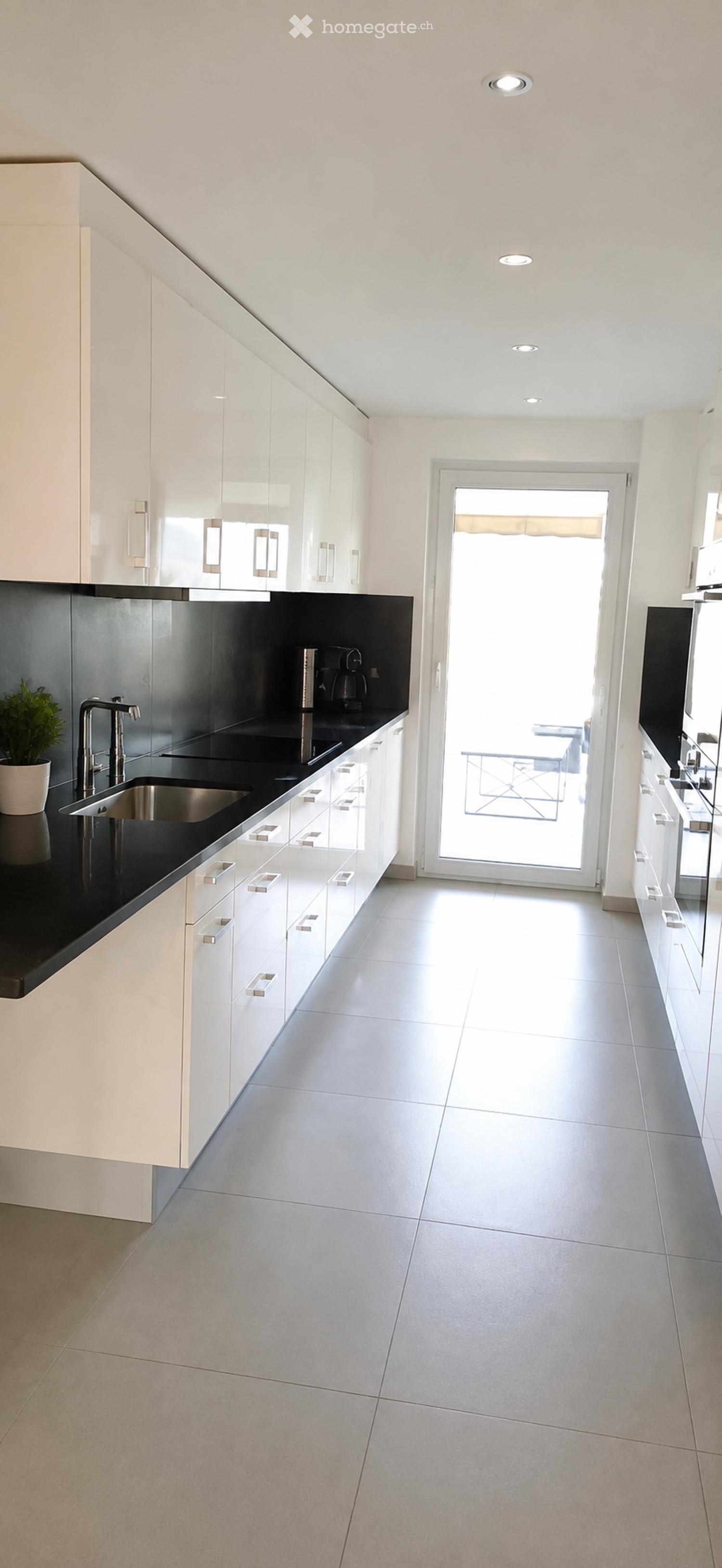 Modern kitchen with white cabinets, black countertops, stainless steel sink, and a view through a large glass door.