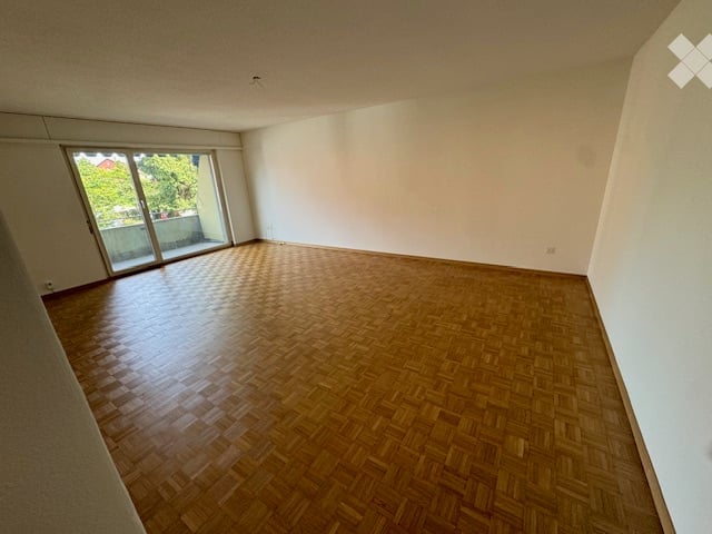 Empty room with wooden parquet flooring, white walls, and large sliding glass door leading to a balcony.