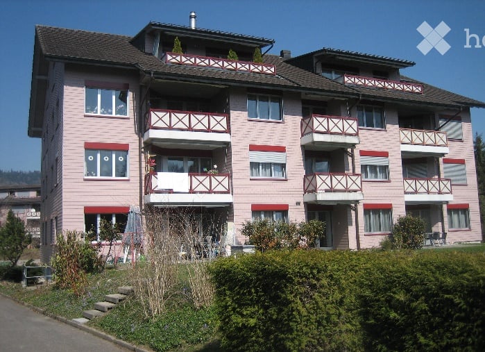 Multi-story residential building with pink facade, multiple balconies, and white window frames.