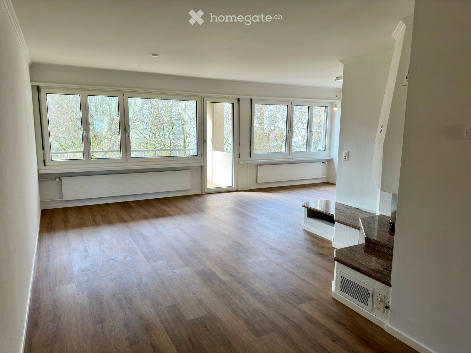 Empty room with wooden flooring, large windows, and a staircase leading upwards.