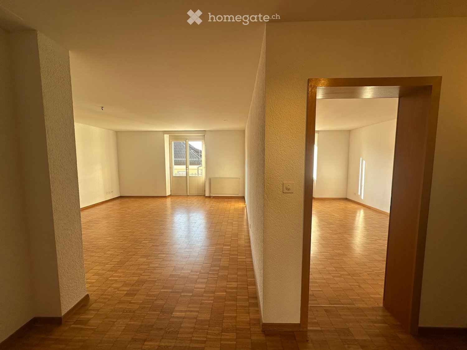 Empty hallway with wooden flooring, white walls, and a door leading to another room.