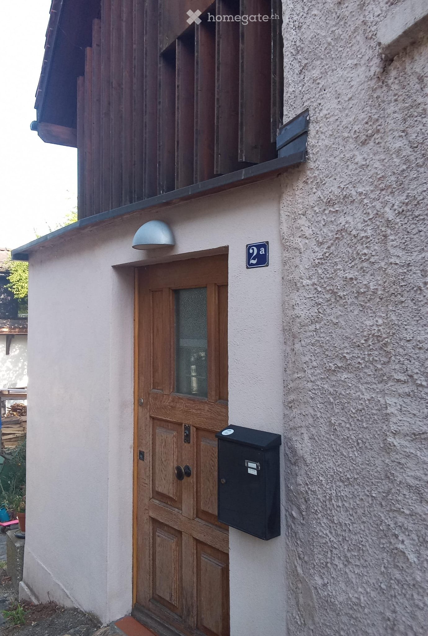 Wooden front door with glass panel, light fixture above, and a mailbox to the right.