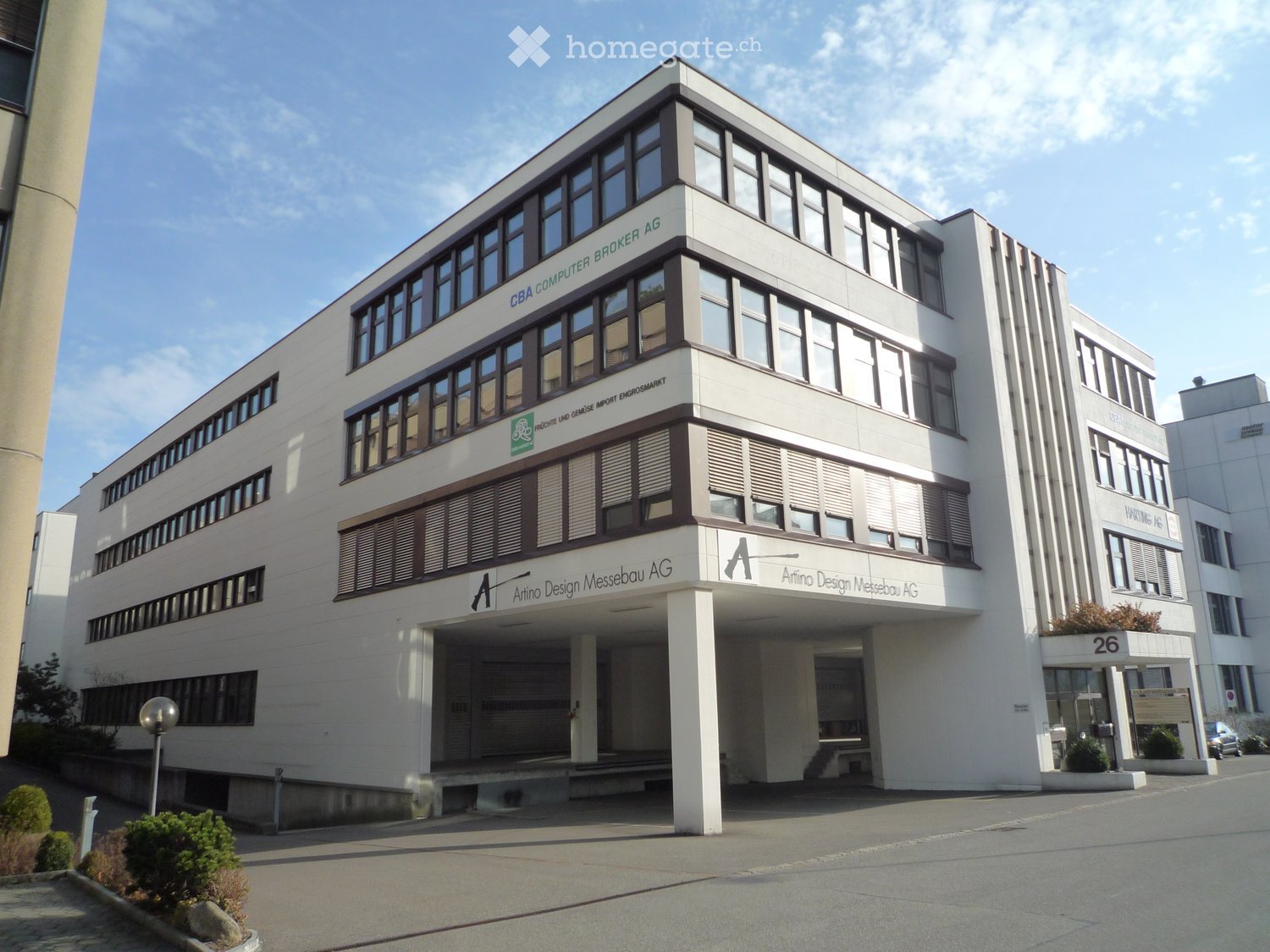 Modern multi-story building with white facade, large windows, and signage for 'Armino Design Messebau AG' and 'CBA Computer Broker AG'.
