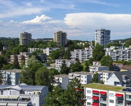 Aerial view of a city with many high-rise buildings, surrounded by trees and greenery.