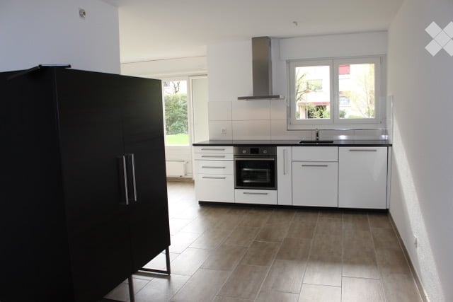 Modern kitchen with white cabinets, black countertops, and a built-in oven. Features a range hood, sink, and faucet, with a large window providing natural light.