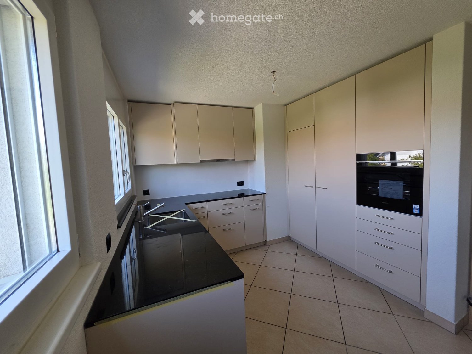 Modern kitchen with white cabinets, black countertop, stainless steel sink, and built-in oven.