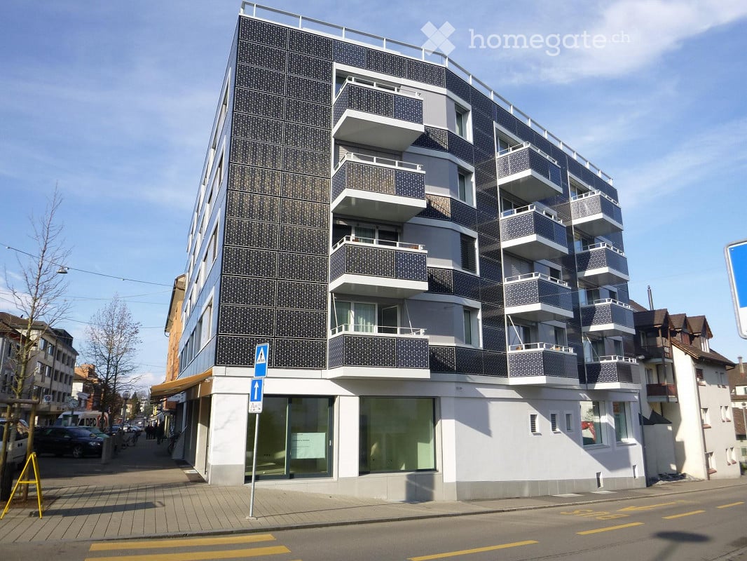 Modern multi-story apartment building with black and white facade, multiple balconies, and large windows on the ground floor.