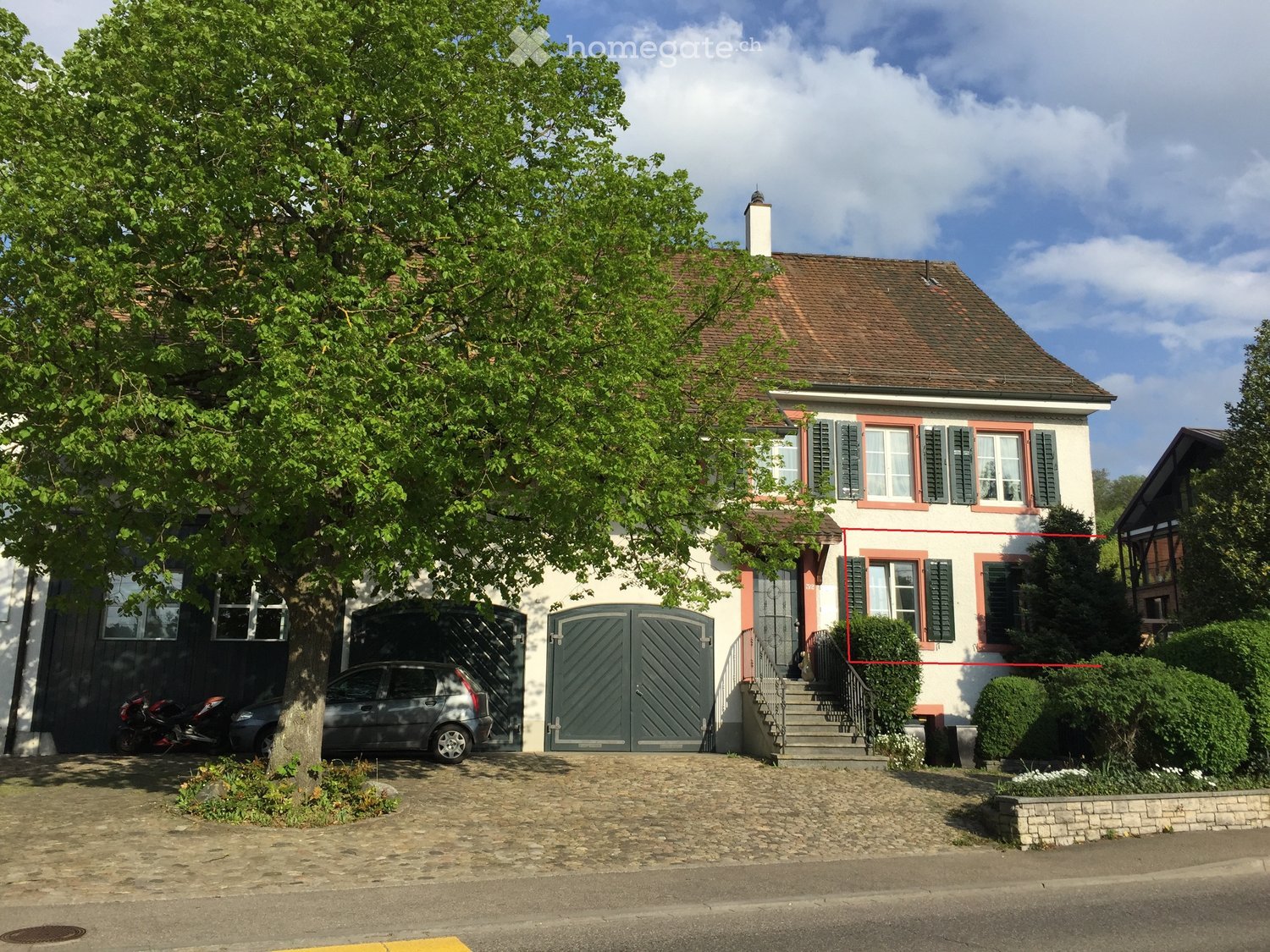 House with a brown roof, black shutters, a large driveway, car parked near the entrance, and a motorcycle parked beside the house