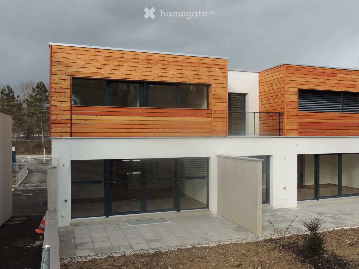Modern two-story house with white and wooden exterior, large windows, and a balcony on the upper level.